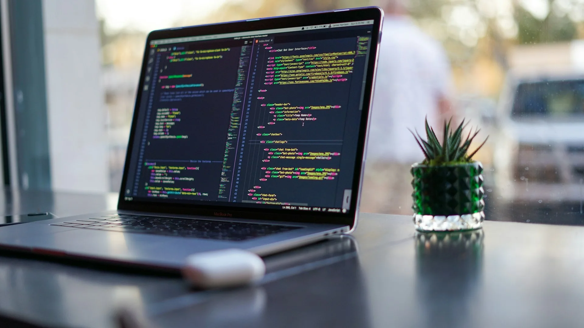Laptop showing code beside a plant in a modern workspace